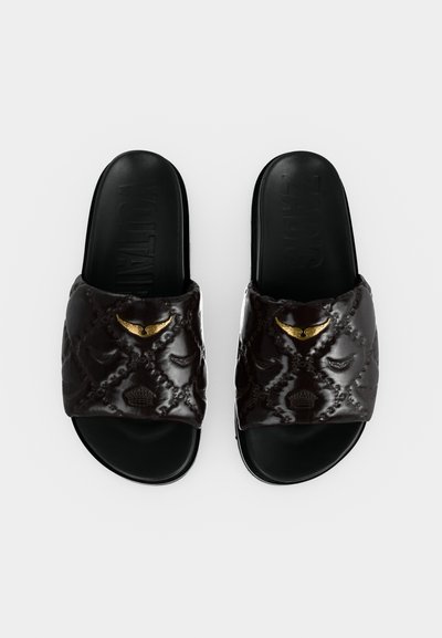 Ζευγάρι μαύρα σανδάλια slide με ραμμένους ιμάντες, διακοσμημένα με ανάγλυφα μοτίβα και μικρά χρυσά διακοσμητικά σε σχήμα φτερού και κορώνας.