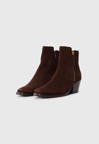 Bottines en daim marron avec un léger talon, dotées d'une fermeture éclair latérale et d'une texture lisse. Design à bout pointu et silhouette minimaliste.