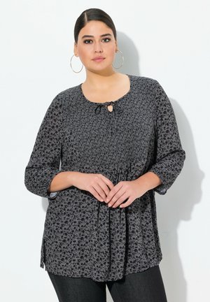 Černá blouse s květinovým vzorem, kulatým výstřihem a detailem ve tvaru klíčové dírky. Má tříčtvrteční rukávy a volný střih.