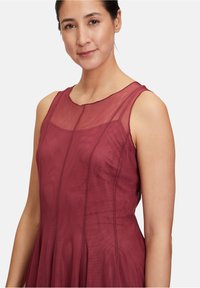 Burgunderfarbenes ärmelloses Kleid mit einem transparenten Netzüberzug, A-Linien-Silhouette und vertikalen Nähdetails für zusätzliche Textur und Design.