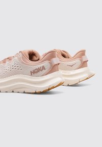 Zapatillas de running de malla rosa claro con acentos blancos, diseño curvado, cuello acolchado y suelas texturizadas. Presentan un logo y tiradores para ponerlas fácilmente.