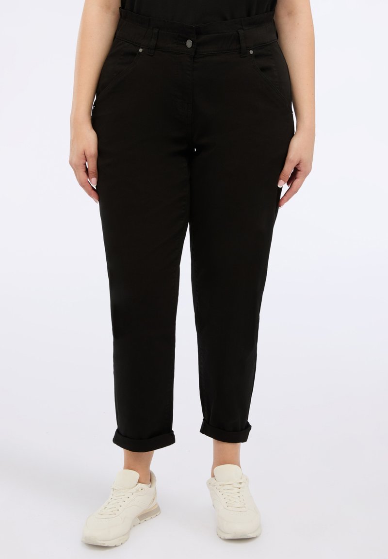 Pantaloni neri a gamba dritta in misto cotone, con chiusura a bottone, cinque tasche e orli rialzati. Indossati con sneakers bianche.
