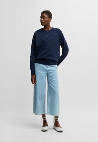 Marinblå sweatshirt med präglade mönster, tillsammans med ljusblå vida jeans. Skorna är ljusgråa med snören.