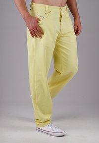 Yellow cotton trousers with a relaxed fit, featuring pockets and a button closure. Paired with white sneakers, showcasing a casual style.