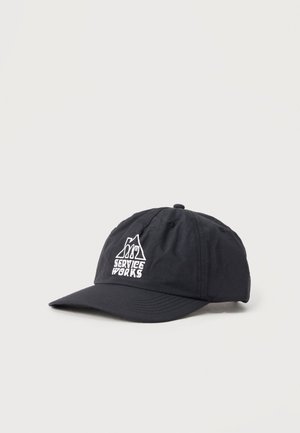 Μαύρο καπέλο μπέιζμπολ με λευκό λογότυπο «Service Works» που απεικονίζει ένα βουνό και σκεύη μπροστά, παρουσιασμένο σε απλό φωτεινό φόντο.