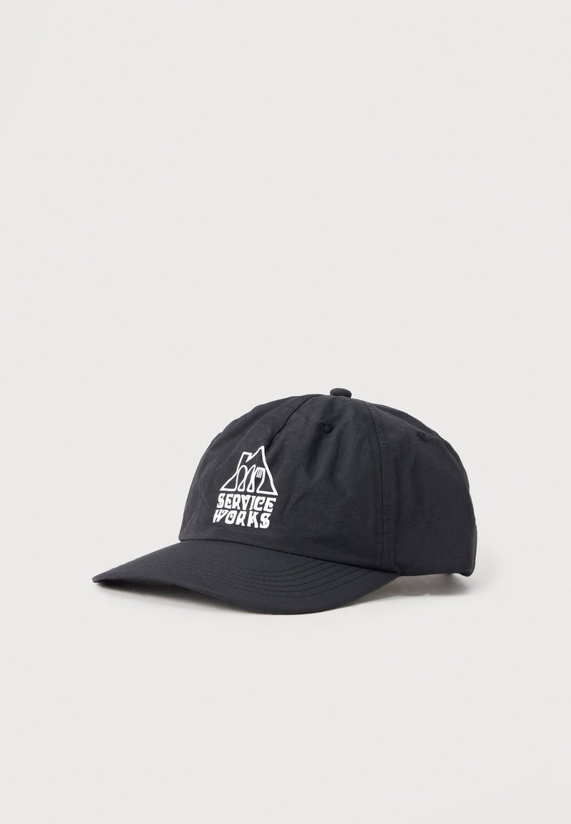 Μαύρο καπέλο μπέιζμπολ με λευκό λογότυπο «Service Works» που απεικονίζει ένα βουνό και σκεύη μπροστά, παρουσιασμένο σε απλό φωτεινό φόντο.
