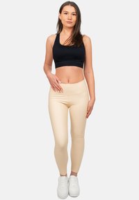 Top sportivo nero accoppiato con leggings beige a vita alta, caratterizzati da una texture liscia. La modella indossa scarpe da ginnastica bianche.