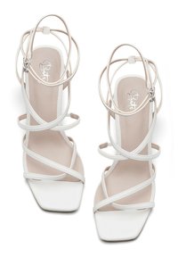 White high-heeled sandals featuring a square toe, thin crisscross ankle straps, and a smooth, matte texture on the sole.