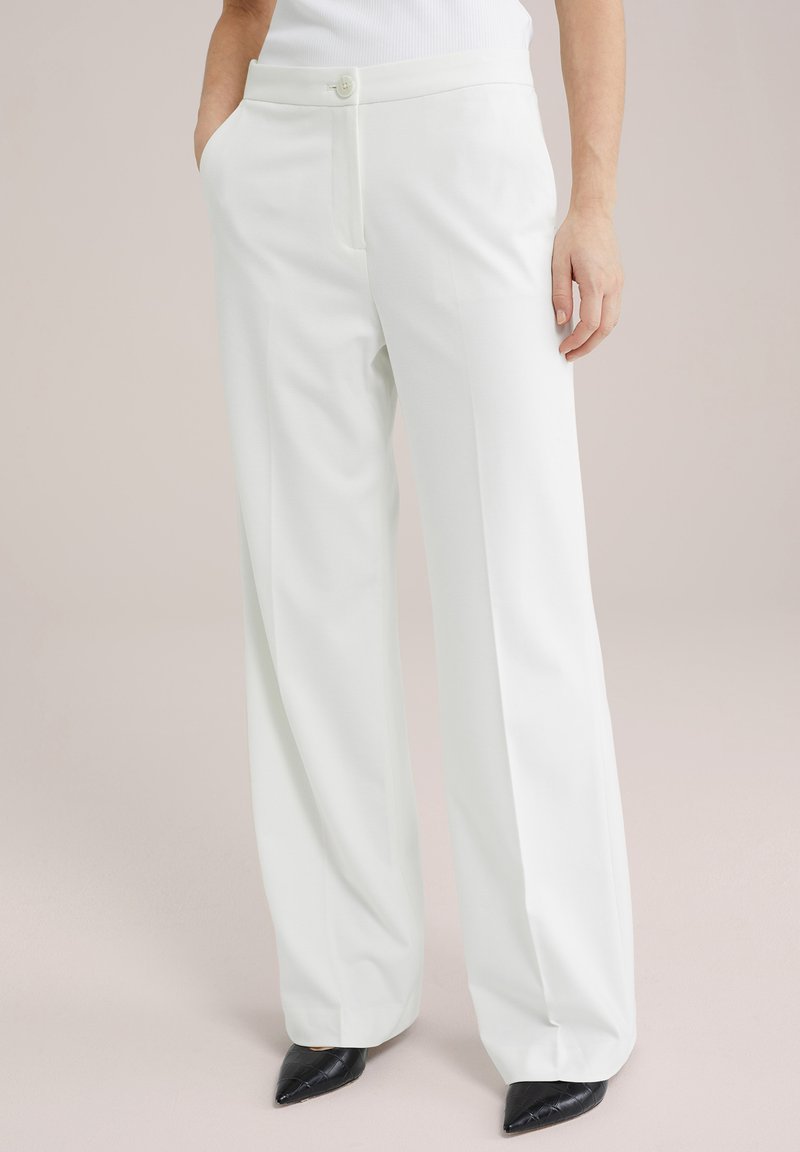 Pantaloni bianchi a gamba larga con chiusura a bottone, tasche laterali e una trama morbida e liscia. Abbinati a scarpe nere a punta.