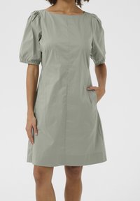 Ljusgrön, knä-length klänning med fyrkantig halsringning, puffade korta ärmar och sidofickor; gjord av mjukt, lätt tyg.