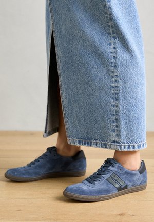 Blaue Wildledersneaker mit einem schwarzen Gummifersenakzent, strukturiertem Obermaterial und Schnürsenkeln. Kombiniert mit einem hellen Denim-Rock mit einem seitlichen Schlitz.