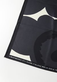 Silketørklæde med en markant sort baggrund og et abstrakt beige blomsterdesign. Kanterne er omhyggeligt syet, med logo langs den nederste kant.