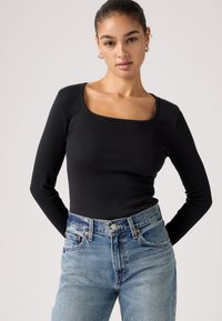 Μαύρο, μακρυμάνικο ριμπ τοπ με τετράγωνη λαιμόκοψη, συνδυασμένο με ψηλόμεσο ανοιχτόχρωμο τζιν τζιν με ορατές ραφές και ξεθωριασμένα σημεία.