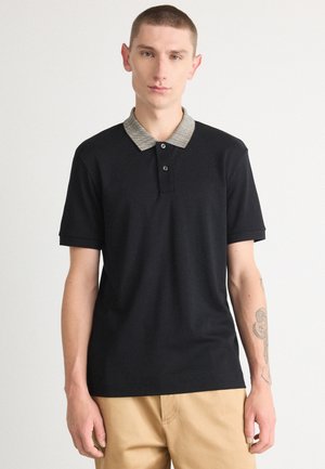 Polo negro hecho de una tela suave, con un cuello texturizado gris, tapeta de dos botones y mangas cortas.