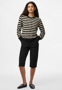 Randig stickad cardigan i beige och svart, med rund hals, knäppning fram och ribbade ärmslut. Kombinerad med skräddarsydda svarta shorts och slip-on skor.