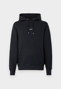 Sudadera negra con bolsillo frontal, capucha con cordón y logo blanco "GANT" centrado en el pecho sobre un fondo liso.