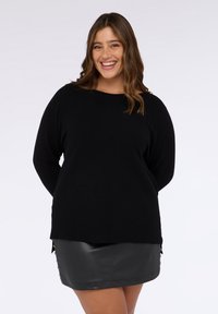 Maglione nero in maglia con maniche lunghe, scollo rotondo e trama a coste. Abbinato a una gonna in pelle nera con bottoni laterali.