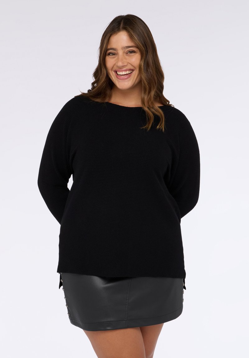 Maglione nero in maglia con maniche lunghe, scollo rotondo e trama a coste. Abbinato a una gonna in pelle nera con bottoni laterali.