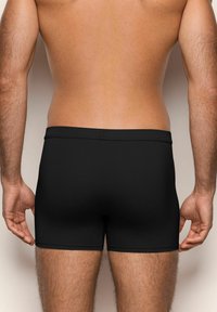 Trunchi de �înot negri, din material moale, cu o potrivire strânsă și un design simplu, fără modele, văzuți din spate.