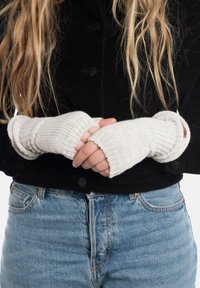 Guanti senza dita bianchi in maglia con una texture a costine, indossati con una giacca nera in corduroy, che rivelano parzialmente dei jeans in denim azzurro chiaro.