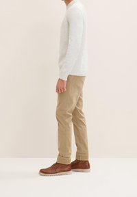 Jasnoszary dzianinowy sweter, beżowe chinosy i brązowe skórzane buty z teksturowanymi akcentami. Widok z boku, prezentujący casualowe połączenie stroju.