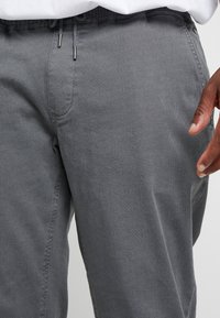 Harmaat, kuvioidut housut, joissa on hienovarainen hunajakennokuvio, joustava vyötärönauha kiristysnyörillä ja sivutaskut.