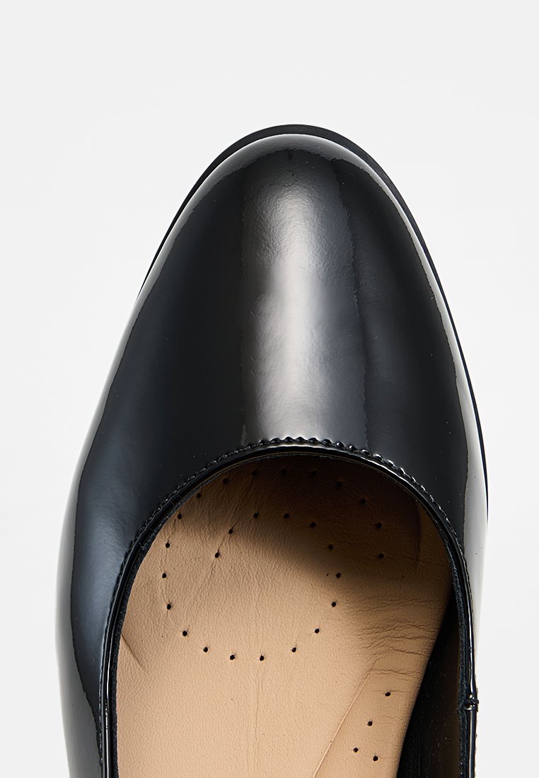 Schwarze Lacklederschuhe mit runder Spitze, glattem, glänzendem Obermaterial und perforierter, tanfarbener Innensohle. Mit feinen, gesteppten Details versehen.