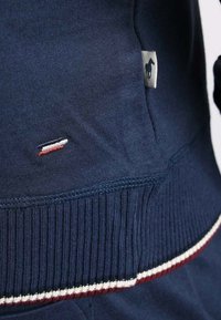Pull en bleu marine avec une texture côtelée, doté d'une petite étiquette logo et d'une bande contrastante rouge et blanche le long du bas.