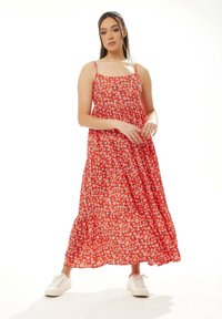 Red floral maxi dress with thin straps, gathered bodice, and tiered skirt. Worn with white sneakers for a casual look.