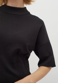 Černý top s krátkým rukávem a vysokým výstřihem, vyrobený z elastického materiálu. Má jemné švy a hladkou texturu.