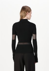Top nero a maniche lunghe con texture a costine, caratterizzato da pannelli in rete trasparente alle maniche e in vita. Design con colletto e silhouette aderente.