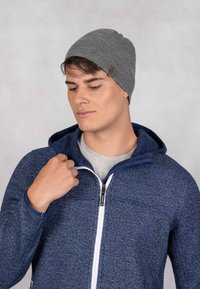 Szara dzianinowa czapka beanie o gładkiej strukturze, zestawiona z niebieską bluzą z zamkiem błyskawicznym, która ma kontrastowy biały zamek i teksturowaną tkaninę.