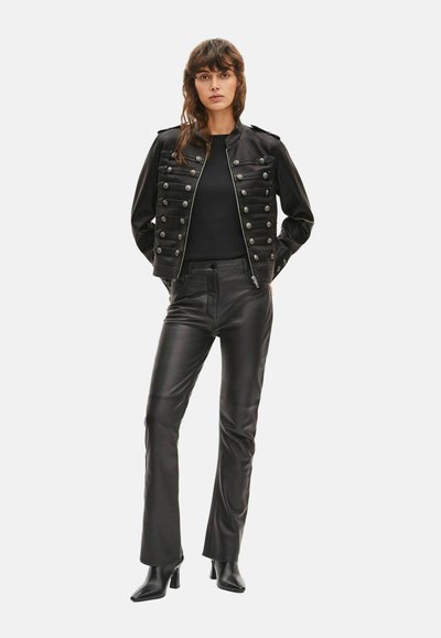 Veste militaire en cuir noir avec boutons décoratifs, associée à un pantalon en cuir noir ajusté et des bottes noires à talons pointues.