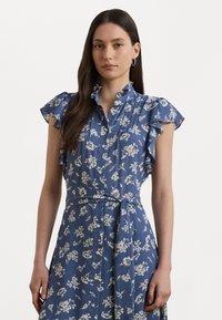 Blue floral dress with ruffled short sleeves, a button-down front, a belted waist, and a soft, flowing fabric. Floral pattern in cream.