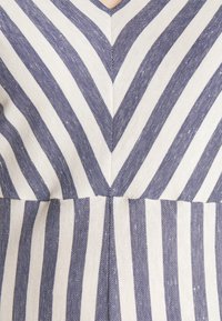 Gros plan d'un tissu avec des rayures verticales bleues et blanches en forme de chevrons formant un V à la couture centrale.