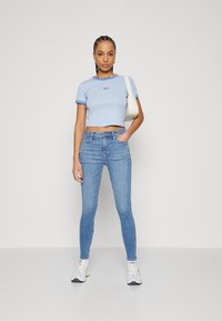 Lyseblå cropped t-skjorte med kontrasterende blå detaljer og logo, kombinert med lyseblå skinny jeans og hvite joggesko med svarte aksenter.
