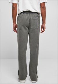 Pantalons de survêtement gris clair avec une taille élastique, fentes latérales au niveau des chevilles et une poche plaquée sur le côté droit. Texture lisse et douce.