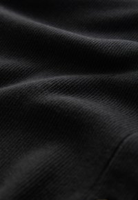 Gros plan sur un tissu noir côtelé avec des plis doux et une texture fine, montrant le motif tricoté et des reflets lumineux subtils.