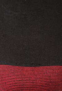 Schwarzer Strickstoff mit einem roten Rippenband am unteren Ende, das ein strukturiertes Muster aufweist. Der Stoff wirkt weich und flexibel.