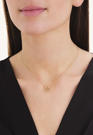 Gros plan sur une femme portant un délicat collier en or avec un pendentif rond décoré d'un motif d'arbre sur une chaîne fine.