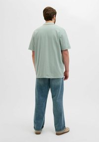 Hele rohelise puuvilla poloshirt lühikeste varrukatega, kombineeritud vabade siniste teksadega. Riietus on klassikalise ja vabalt langeva disainiga.