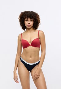 Rode molded beha met verstelbare bandjes en naadloos ontwerp. Zwarte string met witte merkband. Gladde textuur, vormvaste pasvorm.