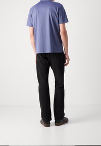 Tričko s krátkým rukávem světle fialové barvy, s rovný střih a bočními rozparky, v kombinaci s černými rovnými džínami a černými pantoflemi.