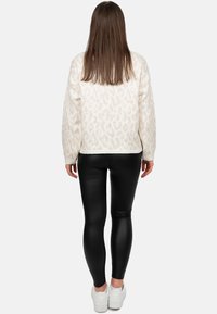 Maglione fuzzy di colore crema con una sottile stampa leopardata, abbinato a leggings neri lucidi e sneakers bianche, visto da dietro.