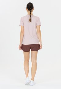 Hellrosa T-Shirt mit kurzen Ärmeln, kombiniert mit braunen Sportshorts, die einen lockeren Sitz und eine weiche Textur bieten. Getragen mit weißen Sportschuhen.