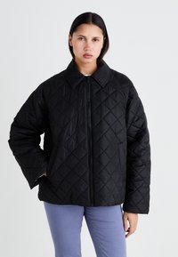 Veste matelassée noire avec un col, dotée d'une fermeture éclair sur le devant et d'une coupe oversize, fabriquée en matériau lisse et léger.
