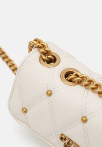 Valkoinen tikattu nahkalaukku kultainen ketjuhihna, jossa metallirenkaat, lyhyet niitit ja logoyksityiskohta pohjassa.