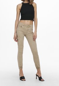 Beige cargobyxor med elastiska muddar, framfickor och en slät yta. I kombination med en svart ribbad crop top och svarta klackskor.