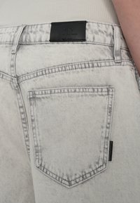 Gaiši pelēki džinsi no denima ar nolietotu tekstūru, ar aizmugurējo kabatu un melnu ādas birku ar tekstu "A|X Armani Exchange".