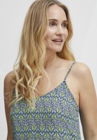 Camisole à motif floral bleu marine avec des accents verts et bleus. Présente des bretelles fines et un tissu léger, idéal pour les vêtements par temps chaud.